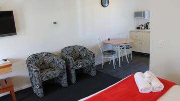 Una habitación con una cama, dos sillones estampados, una mesita, un microondas y un televisor en la pared.