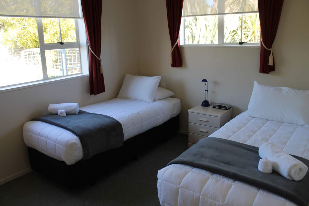 A hotel room with two beds, a nightstand, and a window with curtains.