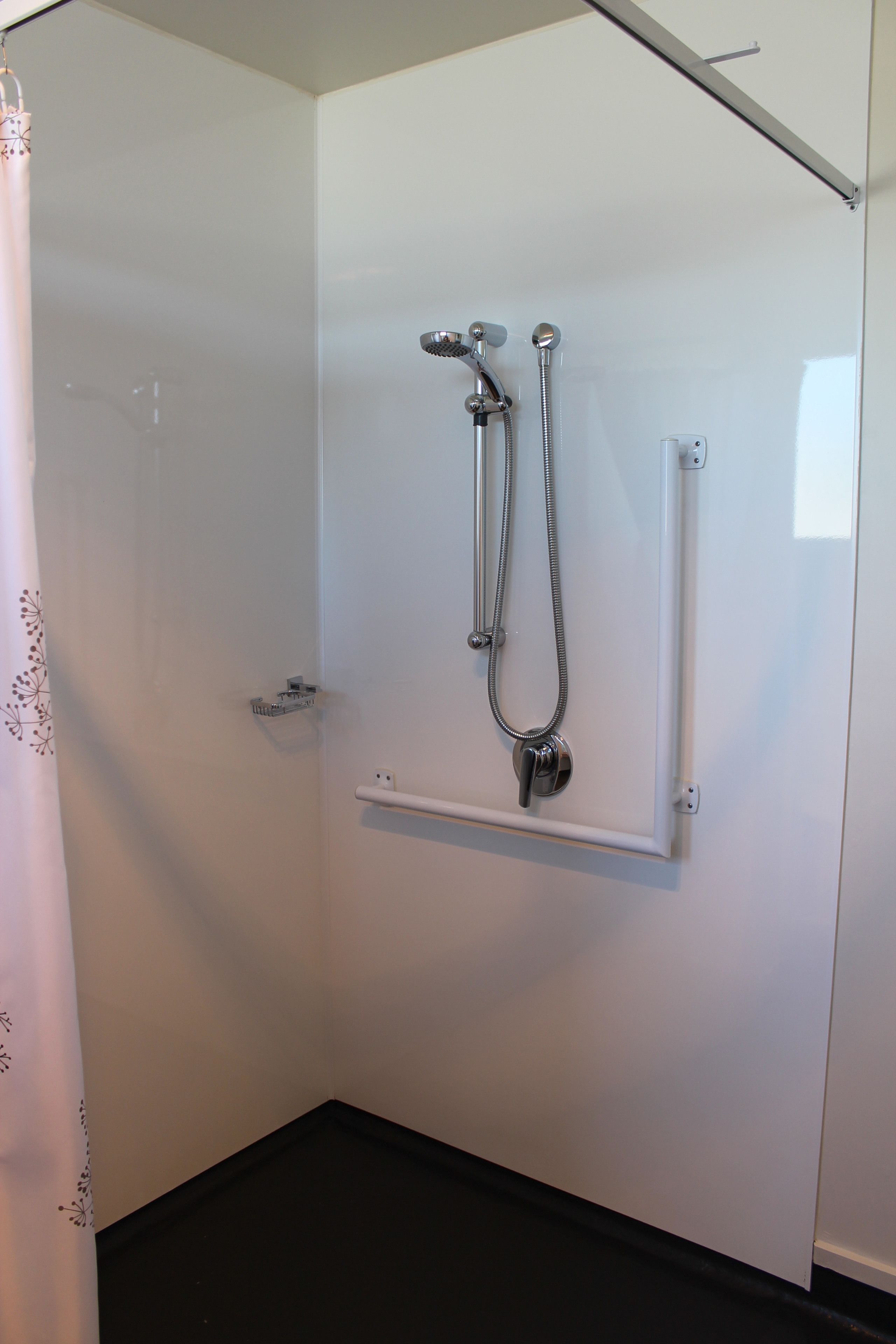 A walk-in shower with a handheld showerhead and a fixed showerhead, a towel rack, and a small shelf.
