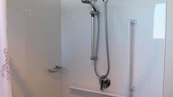 A walk-in shower with a handheld showerhead and a fixed showerhead, a towel rack, and a small shelf.