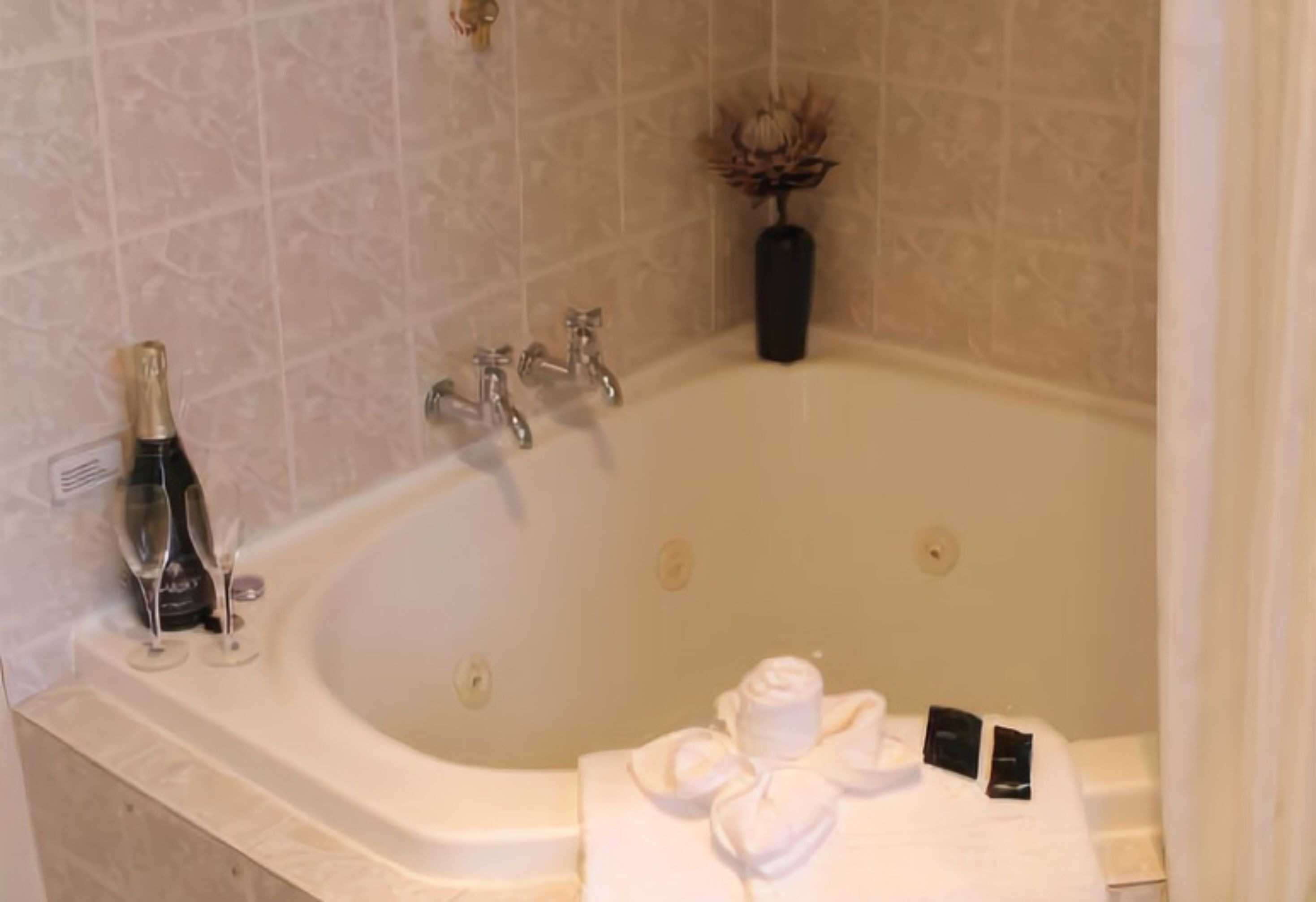 Une salle de bain avec une baignoire, deux coupes à champagne, une bouteille de champagne, une serviette et un petit vase.