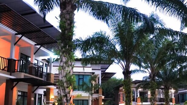 A modern hotel with a swimming pool, palm trees, and a well-maintained garden.