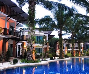 Un hotel moderno con piscina, palmeras y un jardín cuidado.