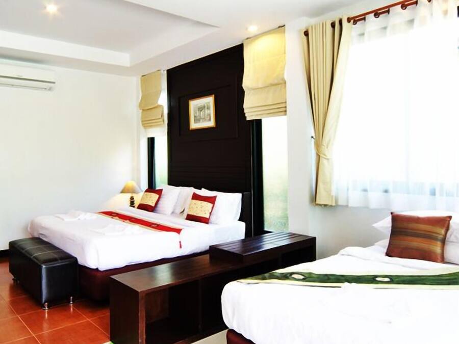 A hotel room with two beds, a wooden nightstand, a small table, and a window with curtains.