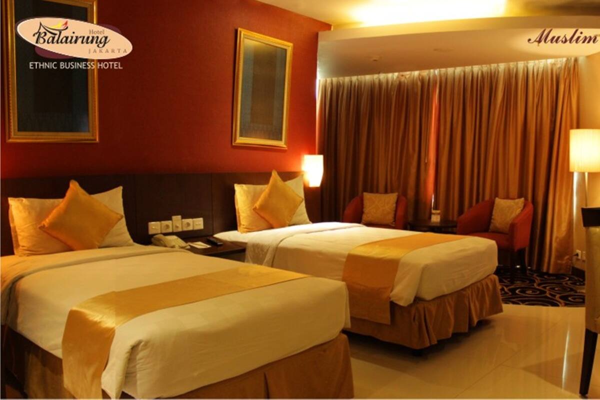 A hotel room with two beds, a desk, a chair, and a large window with curtains.