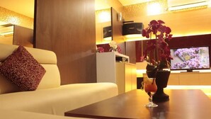 A modern living area with a sofa, a table with a drink, and a TV in the background. - Balairung Hotel (Jakarta)