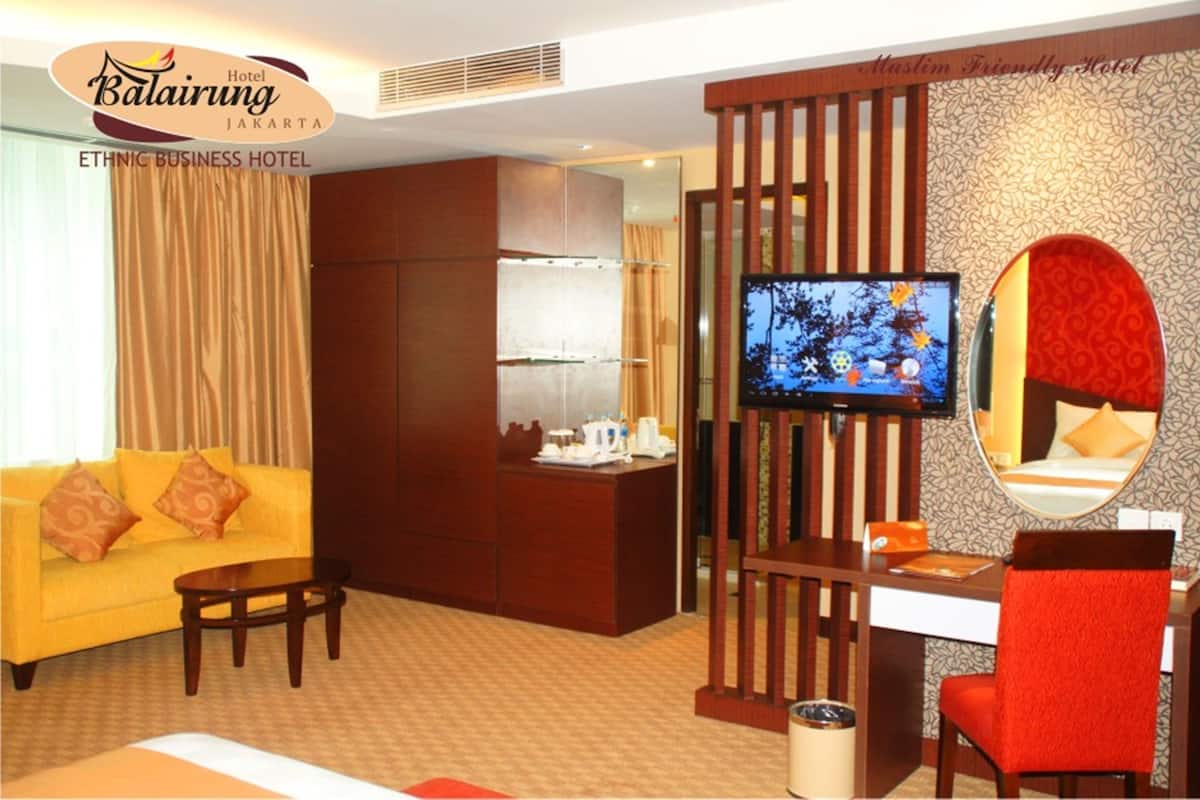 A hotel room with a sofa, a TV, a desk, and a chair.