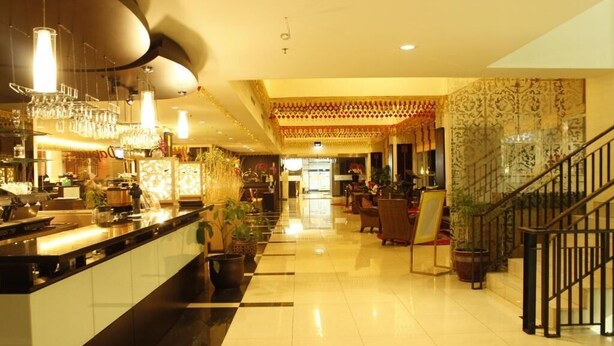 A hotel lobby with a checkered floor, a bar area with a counter and bar stools, and a staircase with a railing. - Balairung Hotel (Jakarta)