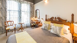 A hotel room with a large bed, a wooden desk, a chair, a mirror, and a nightstand.