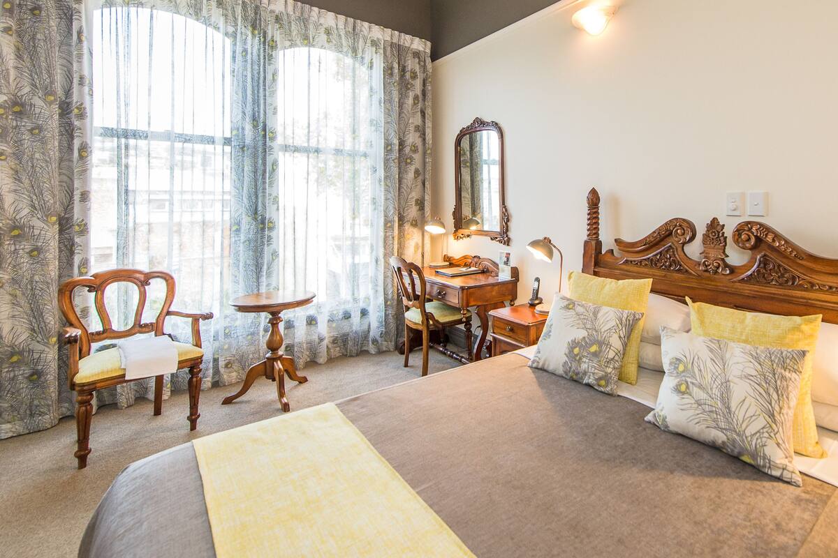 A hotel room with a large bed, a wooden desk, a chair, a mirror, and a nightstand.