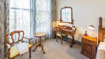 Una habitación con un escritorio de madera, una silla, una mesita, un espejo, una lámpara y una cama.