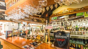 A bar with a Guinness tap, various bottles, and glasses hanging from the ceiling.