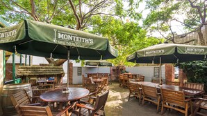 Outdoor dining area with wooden tables and chairs, green umbrellas, and brick walls.
