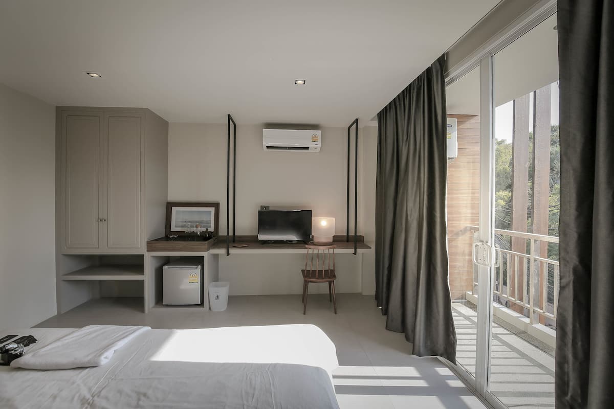 A bedroom with a bed, a desk with a computer, a chair, and a window with curtains.