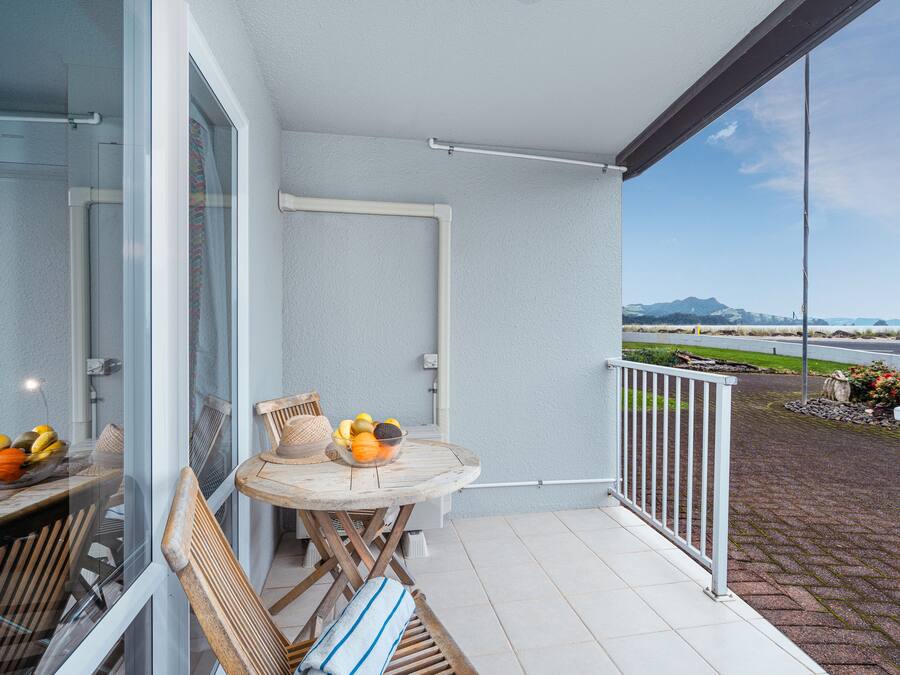 A balcony with a table, chairs, and a bowl of fruit.