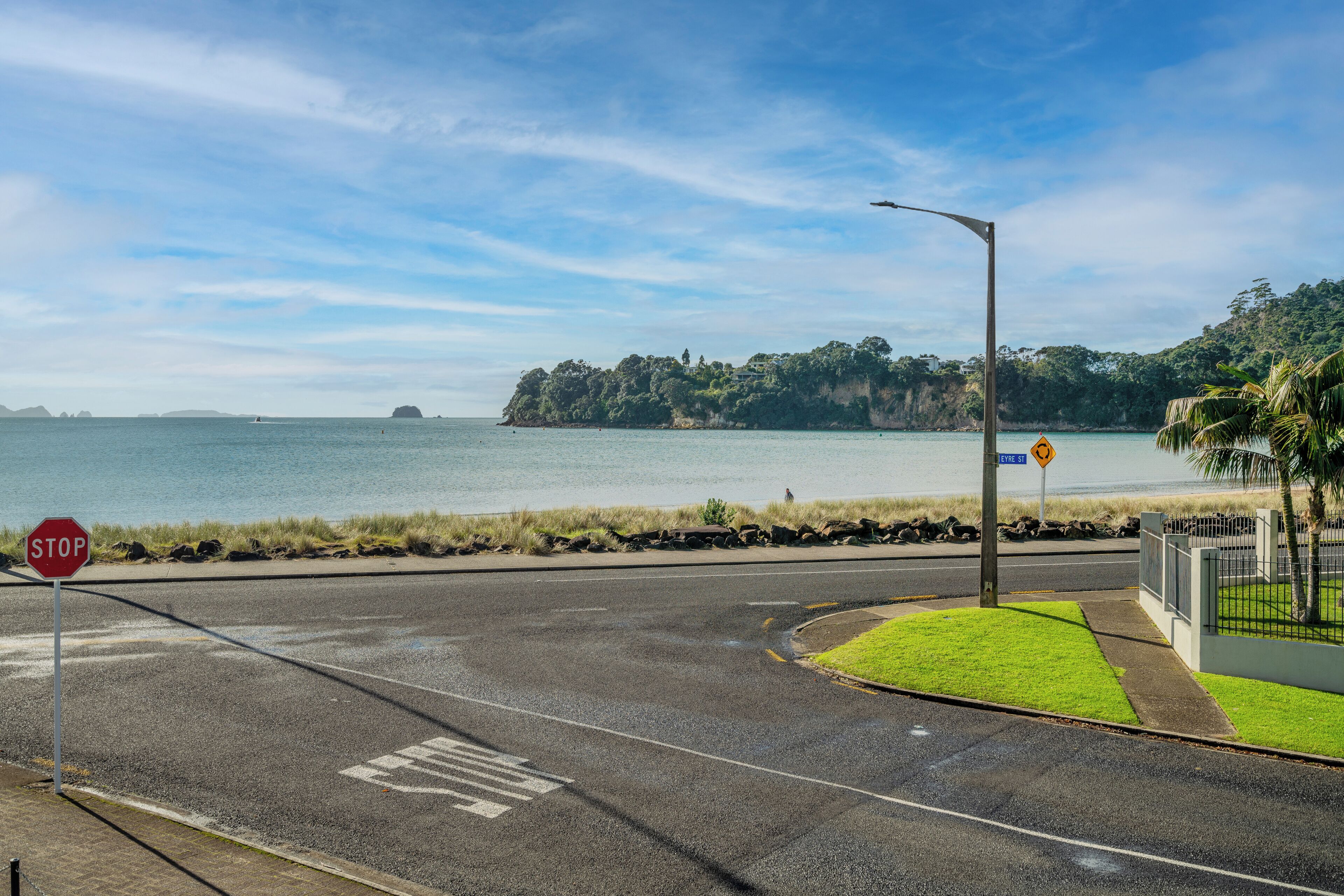 A road with a stop sign and a pedestrian crossing near a body of water.