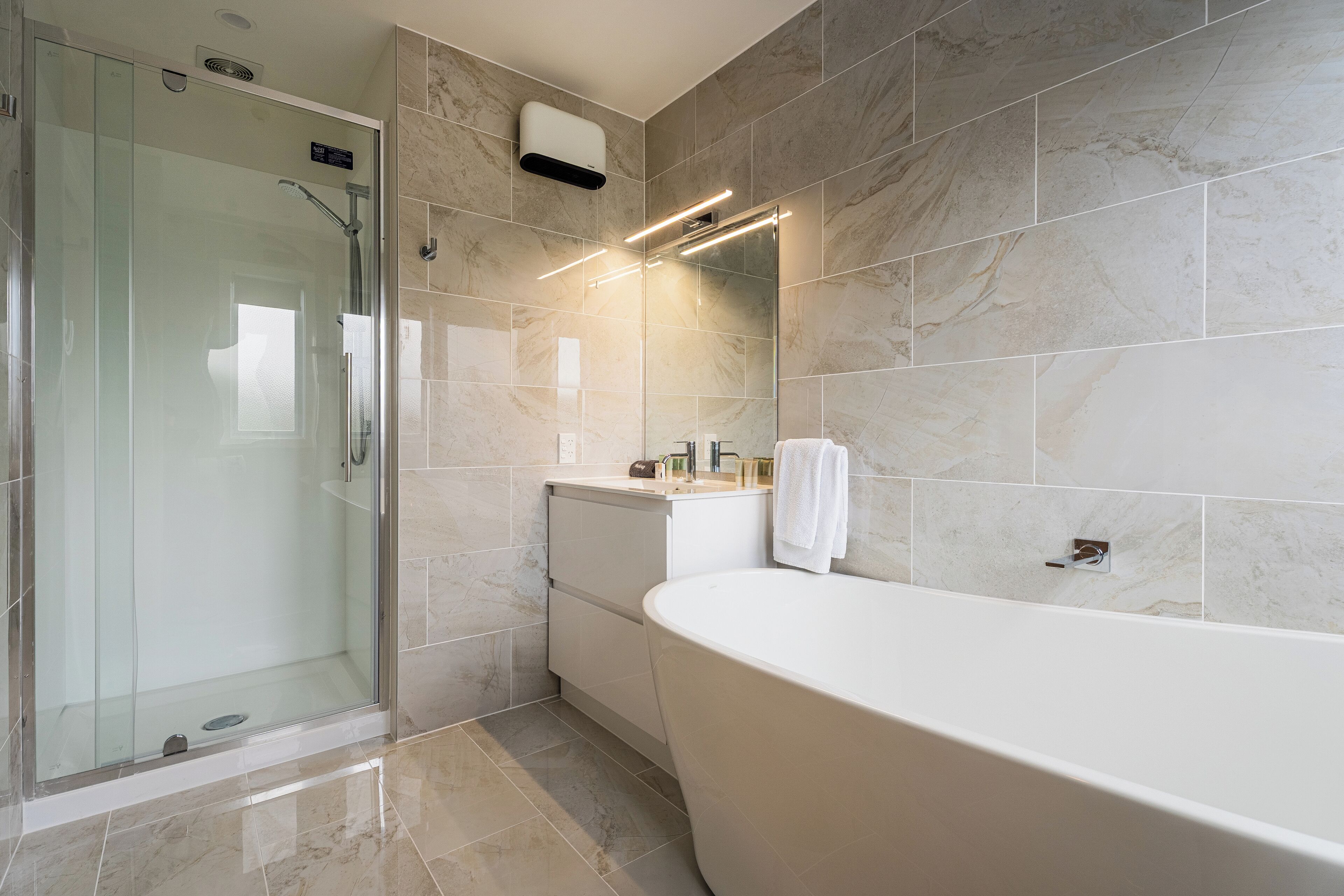 A modern bathroom with a glass-enclosed shower, a freestanding bathtub, and a vanity with a towel hanging on the wall.