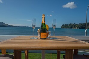 Un tavolo di legno con una bottiglia di champagne Veuve Clicquot Brut, due bicchieri e una ciotola di frutta, con vista su un lago pittoresco.