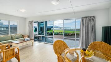 Un salon moderne avec une porte vitrée donnant sur un balcon, des meubles en osier et un panier de fruits posé sur la table.
