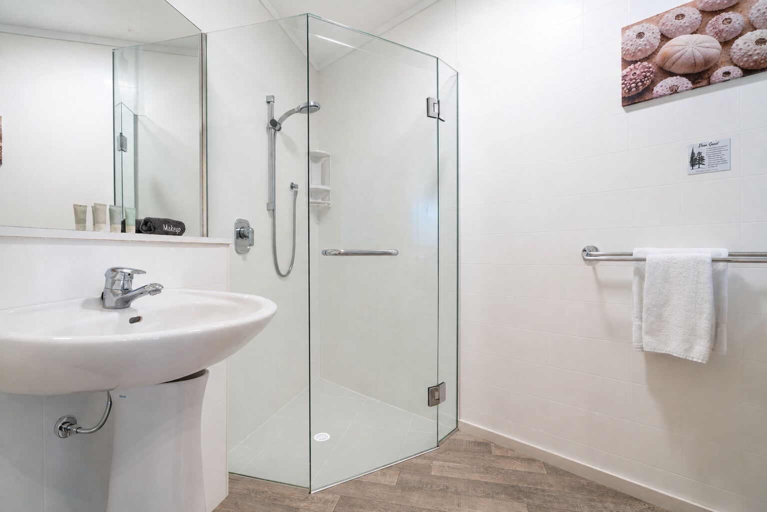 Un baño moderno con ducha de vidrio, lavamanos blanco y toallero.