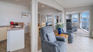Un espacio moderno con sala de estar, cocina, sillones grises, una mesa de comedor y vistas al mar.