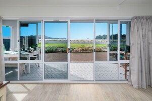 Una habitación con un amplio ventanal corredera que da a un espacio exterior con vistas a un campo verde y montañas.