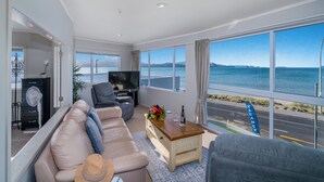 Un salón moderno con un amplio ventanal que ofrece vista al mar y a una carretera.