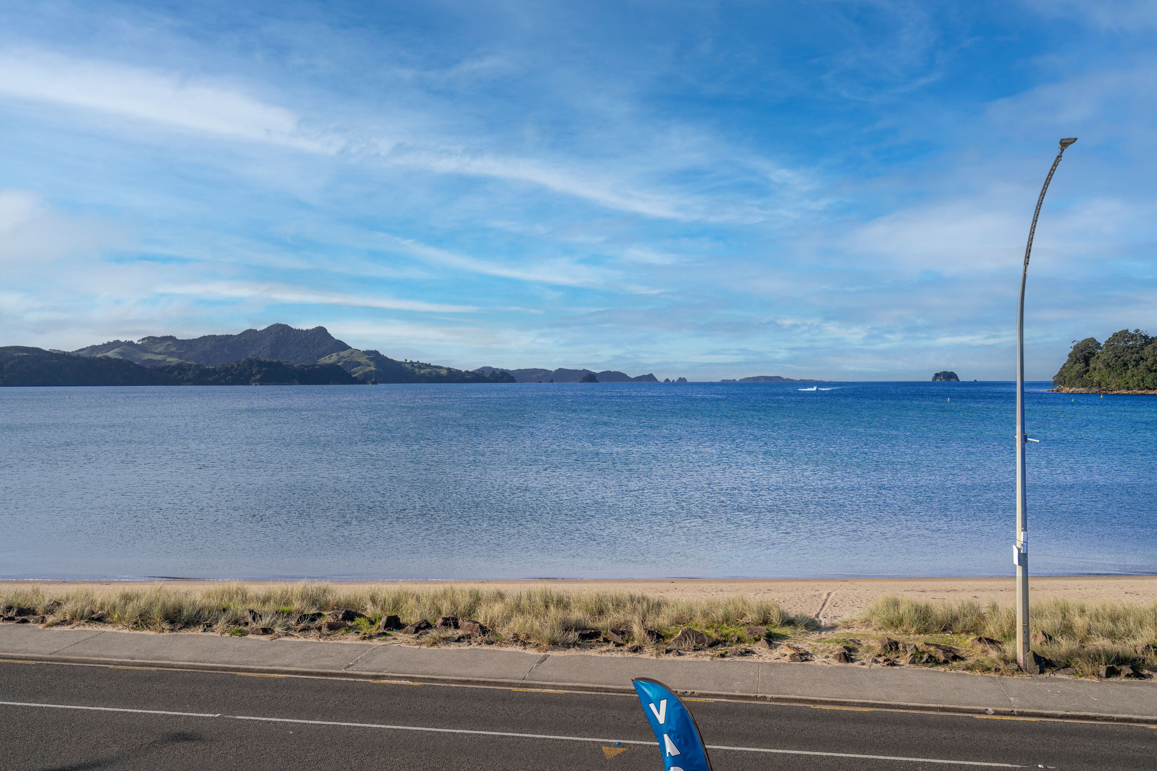 A coastal road with a clear view of the sea and distant mountains.