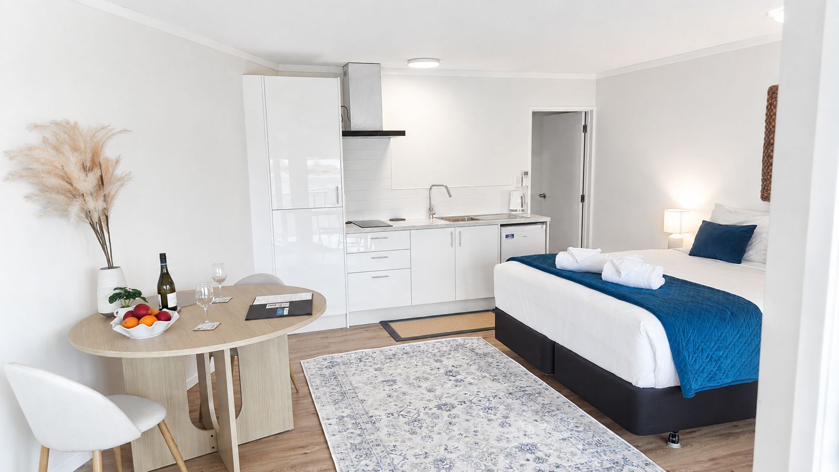 A modern, compact hotel room with a bed, bedside table, and a small kitchenette.