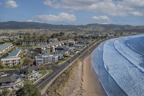 A coastal town with residential buildings, a beach, and mountains in the background.