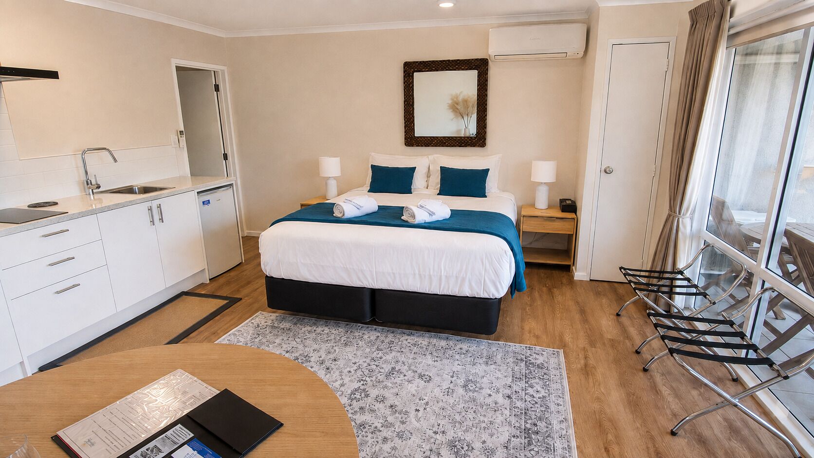 Ein Hotelzimmer mit Bett, Nachttischen, Schreibtisch, Stuhl, Fenster und einer Küchenzeile.