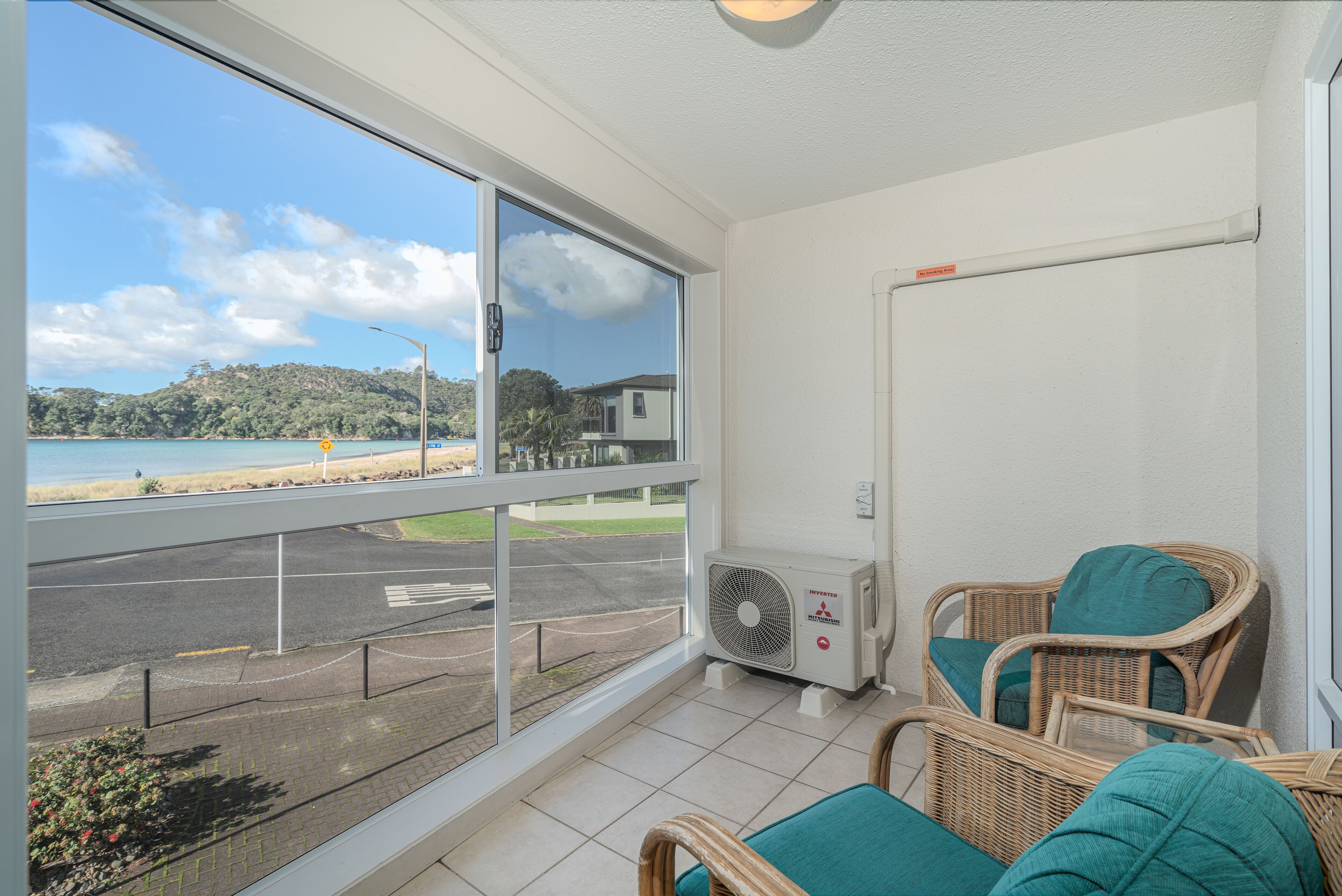 A balcony with wicker chairs, a view of the beach, and a large window.