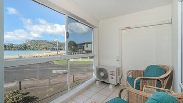 A balcony with wicker chairs, a view of the beach, and a large window.