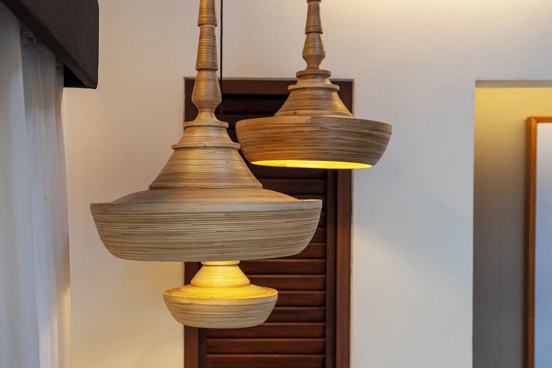 A wooden pendant light fixture with a warm glow, hanging in front of a wooden door.