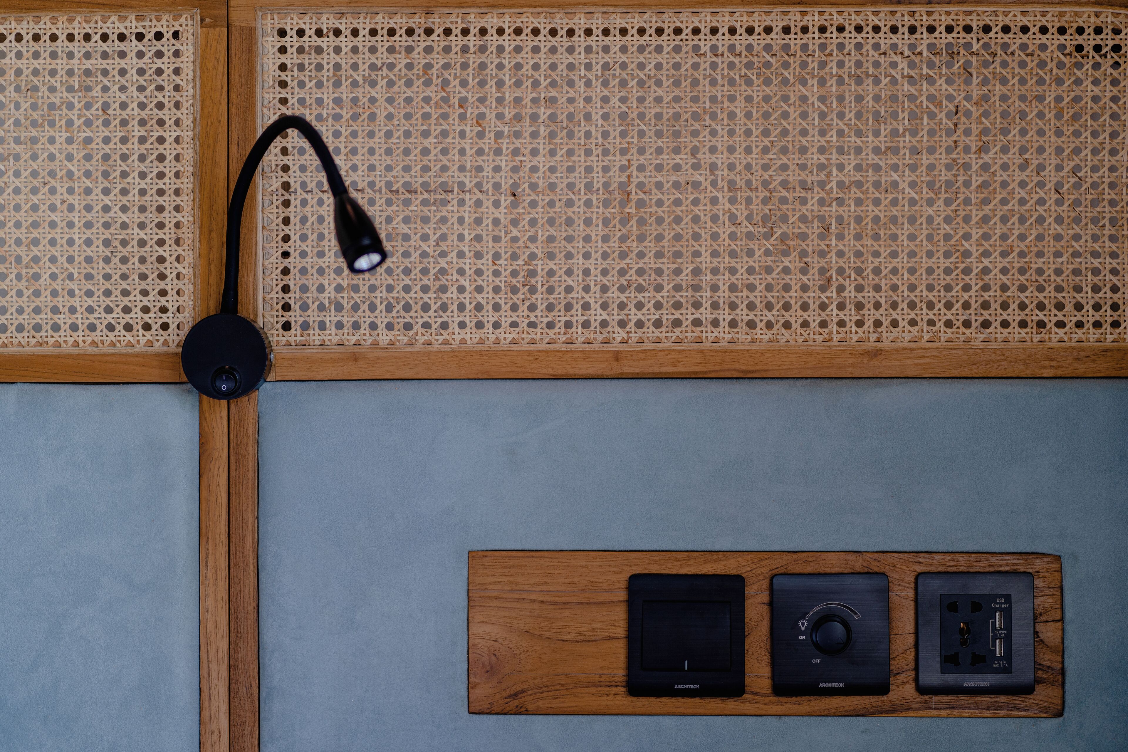 A room with a rattan headboard, a black desk lamp, and a wooden panel with electronic devices.
