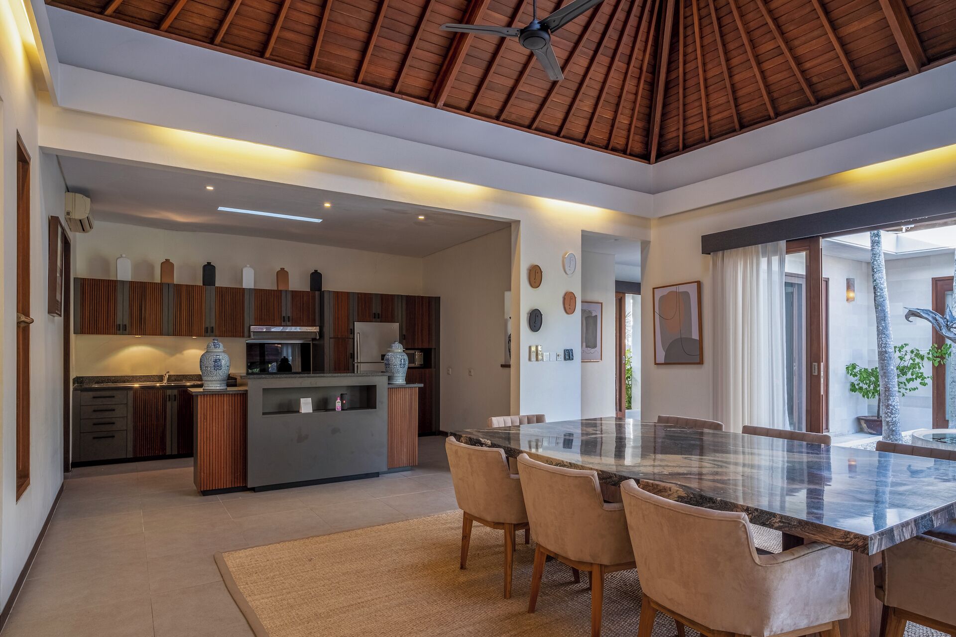 A modern kitchen with wooden cabinets, a central island, and a dining area with a glass-top table and chairs.