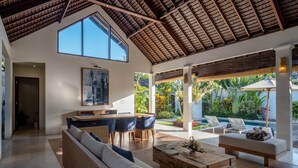 A spacious living area with a high ceiling, a dining area, and a poolside seating area.