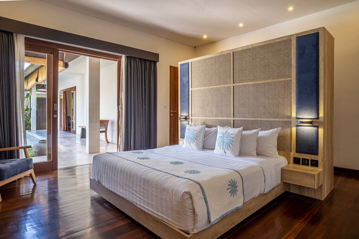 A spacious bedroom with a large bed, a wooden headboard, and a view of an outdoor area.