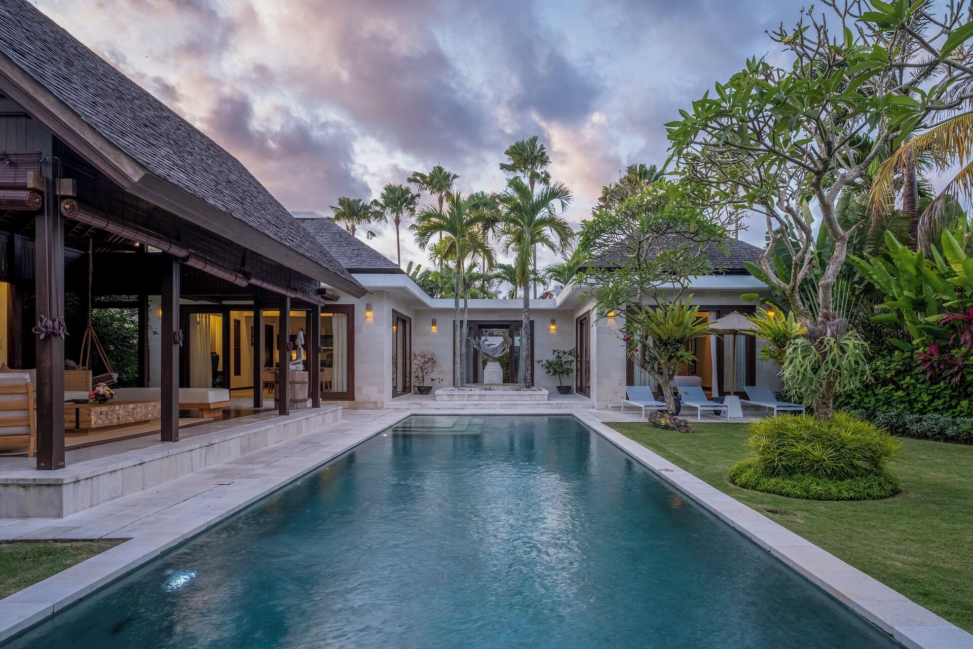 A modern house with a swimming pool, covered outdoor seating, and lush tropical plants.