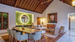 A spacious living area with a high ceiling, a dining table with chairs, a sofa, and a painting on the wall.