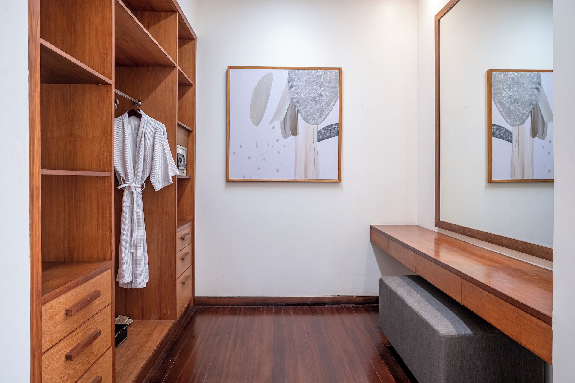 A walk-in closet with wooden shelves and drawers, a gray bench, and a large mirror.