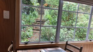 Una mesa de madera con un tapete oscuro y un teléfono inteligente. Una ventana muestra un jardín con plantas y una escalera de madera.