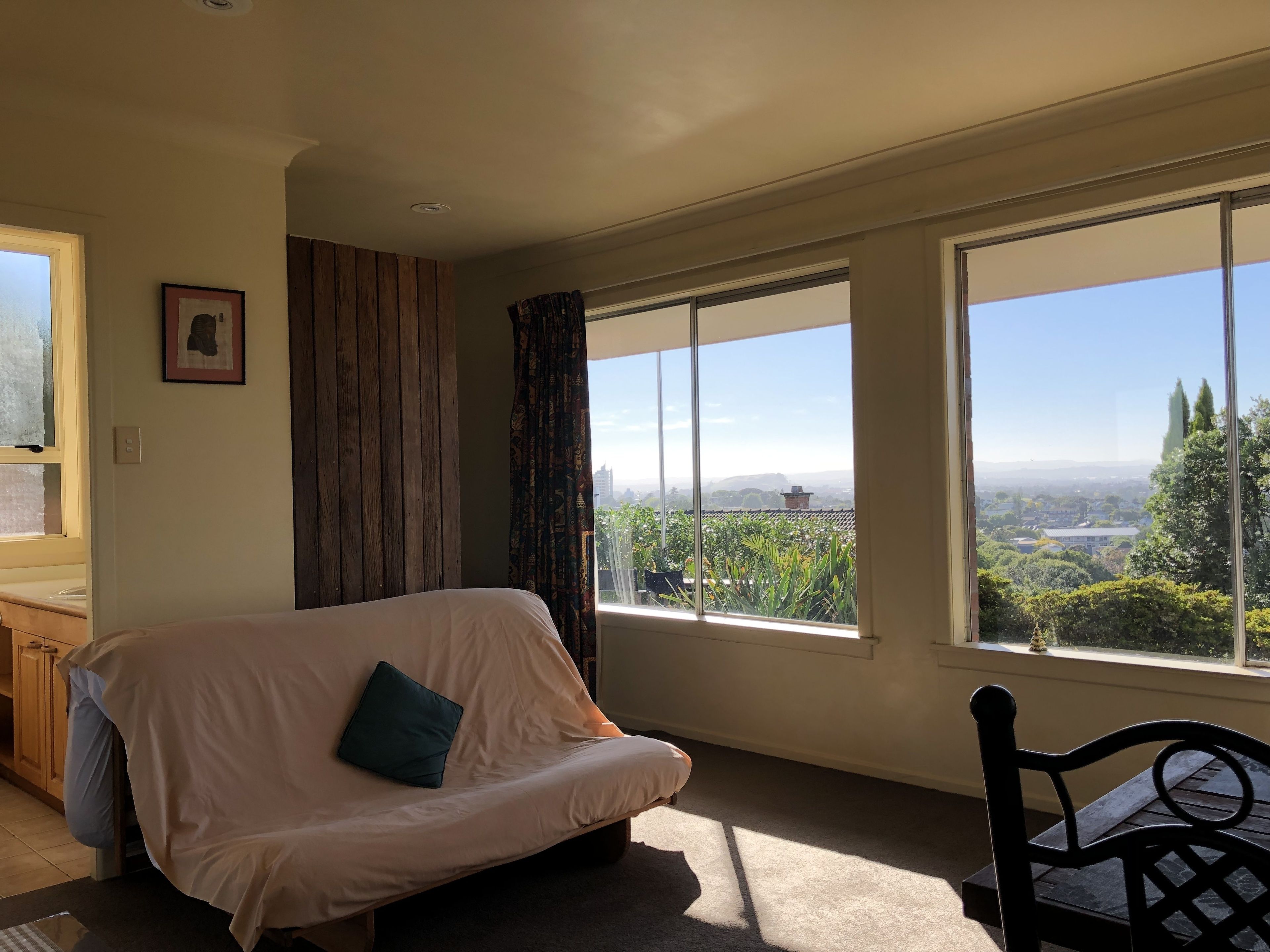 A room with a sofa, a chair, and large windows offering a view of greenery and buildings.