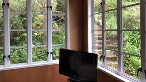 Una habitación con dos ventanas amplias, paredes de madera y una televisión de pantalla plana.