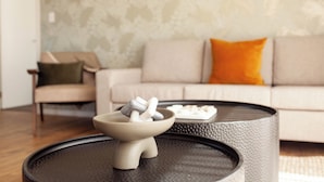 Een moderne woonkamer met een ronde salontafel, een beige bank met oranje kussen en een behang met patroon.