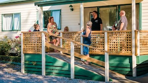 Een overdekte veranda met een houten leuning en treden die leiden naar een huis met witte bekleding en groene accenten.