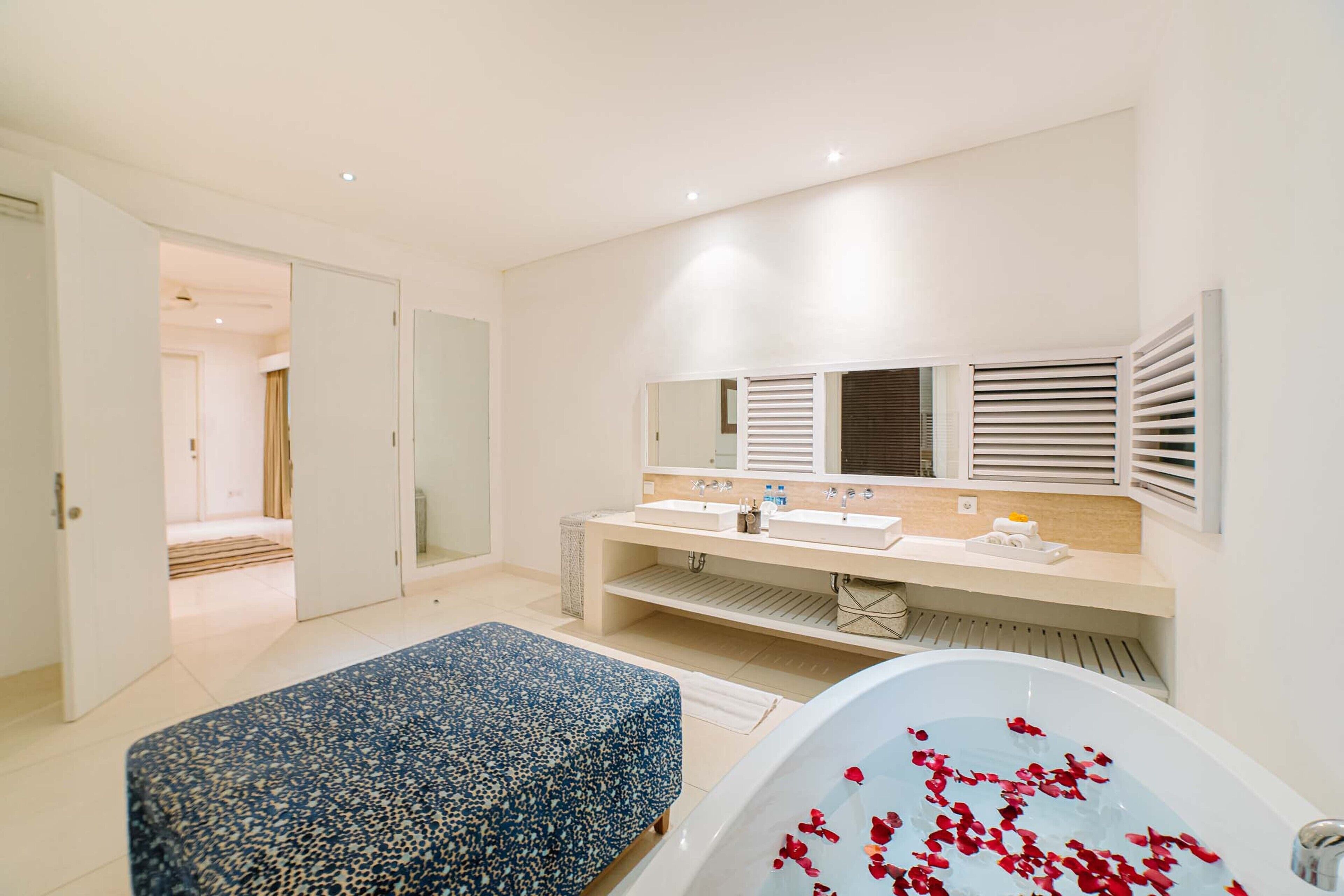 Ein modernes Schlafzimmer mit einem großen Bett, einer Badewanne mit Rosenblättern, einem Doppelwaschtisch und einem begehbaren Kleiderschrank.