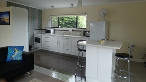 A compact kitchen with a central island, a dining area with a bar stool, and a black sofa with a blue pillow.