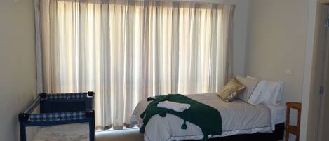 A bedroom with a bed, a small desk, and a window with curtains.