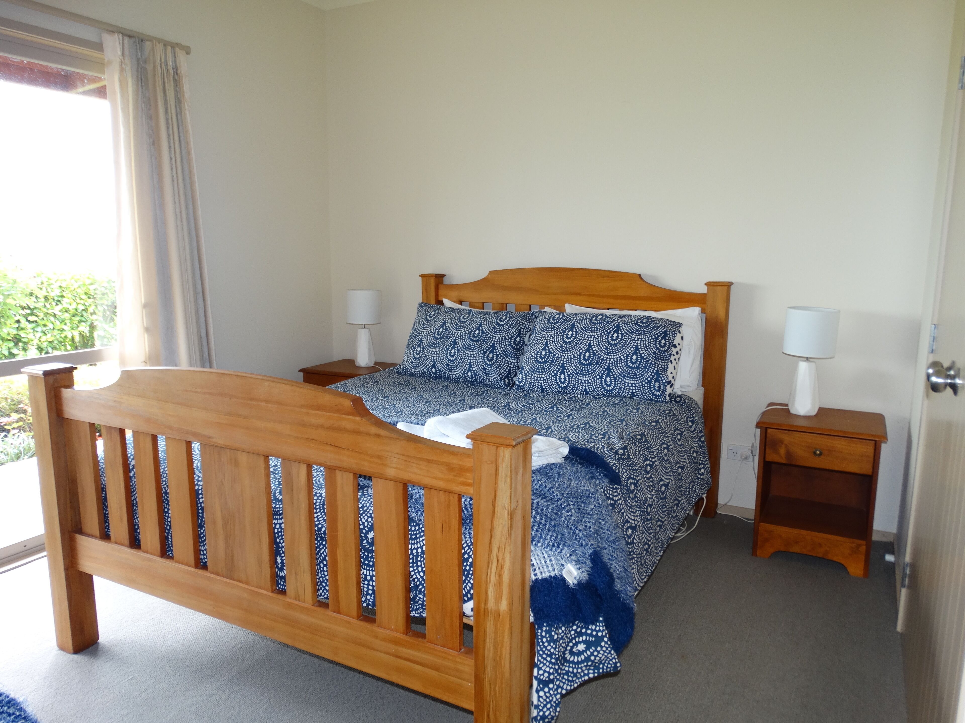 Quarto com cama de madeira, duas mesas de cabeceira e janela com cortinas.